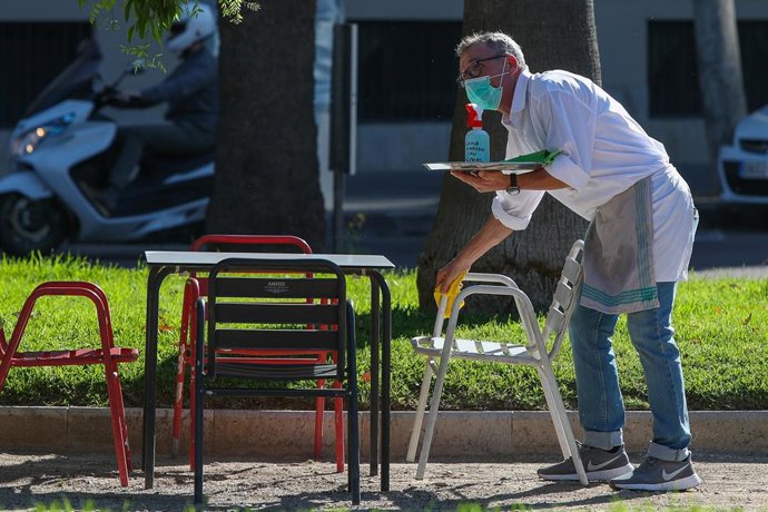 Un camarero limpia las mesas y sillas de una terraza de un bar