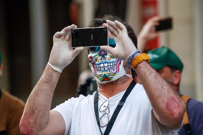 Un hombre con una máscara de calavera toma una fotografía con su móvil durante la manifestación celebrada en la puerta de la sede del PSOE de la calle Ferraz de Madrid, contra la gestión del Gobierno de España contra el coronavirus COVID19 durante la pa