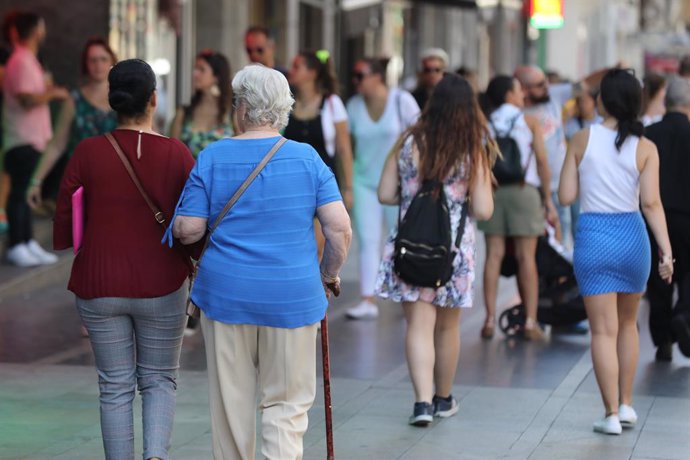 Una dona major passeja del bra d'una altra dona per un carrer de Madrid.