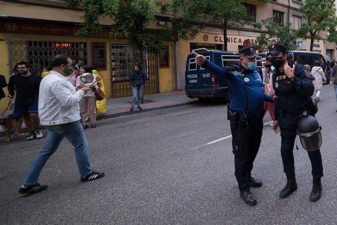 Un Policía Municipal hace indicaciones a un Policía Nacional mientras varias personas se manifiestan en la puerta de la sede del PSOE 