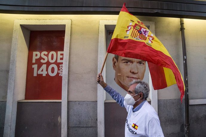 Un hombre alza una bandera de España ante la imagen de Pedro Sánchez en señal de protesta.