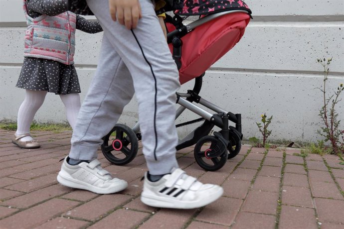 Una niña pasea por la calle empujando un carrito con un bebé de juguete junto a su padre y su hermano