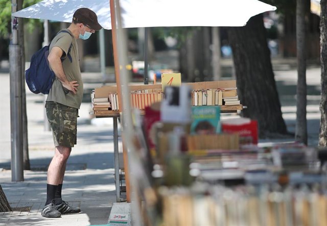 Un hombre protegido con mascarilla observa libros de uno de los puestos en el Mercado de libros de la Cuesta Moyano