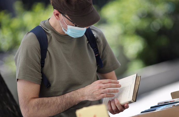 Un hombre protegido con mascarilla observa un libro 