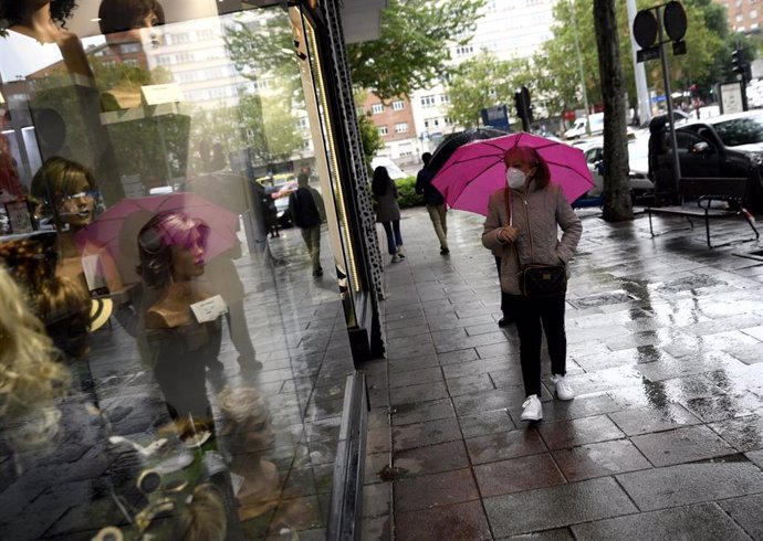 Una mujer pasa frente a una tienda con un paraguas  en un día de lluvia y bajada de temperaturas en toda España