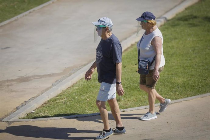 Dos personas con ropa veraniega y gorra pasean por un parque.