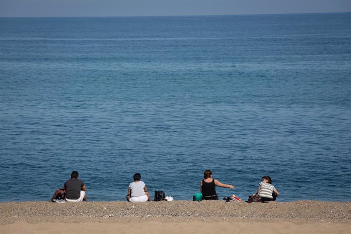 Varias personas sentadas en la Playa de la Barceloneta. 
