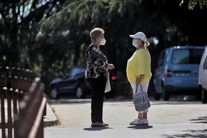 Dos mujeres protegidas con mascarilla mantienen una conversación en la calle.
