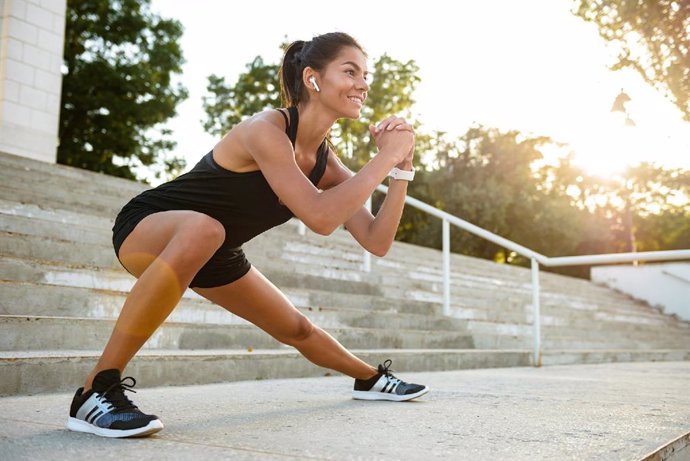 Portrait of a smiling fitness woman in earphones    Portrait of a smiling fitness woman in earphones doing stretching exercises on stairs outdoors