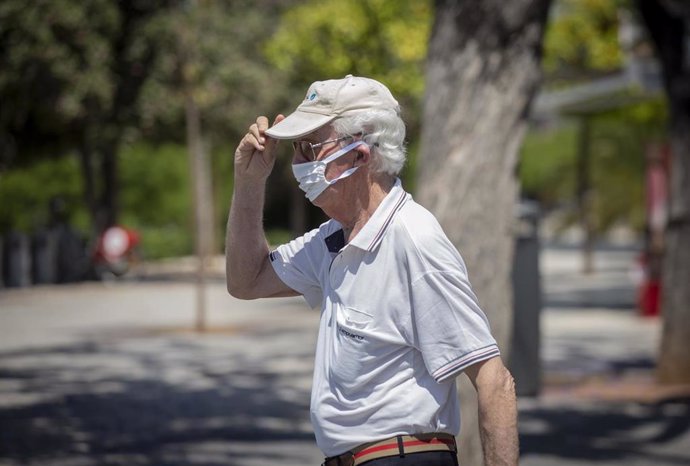 Un hombre con mascarilla y gafas de sol se coloca una gorra.