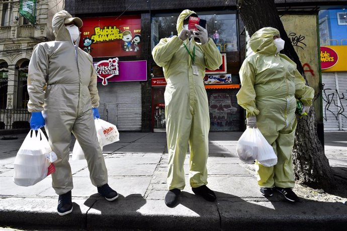 Tres personas ataviadas con trajes protectores en las calles de La Paz tras volver de las compras.