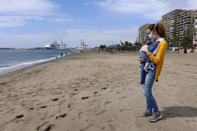 Una mujer protegida con una mascarilla da un paseo con su bebé en la playa de La Malagueta el primer día en el que los menores de 14 años pueden salir, en Málaga (Andalucía ,España) a 26 de abril de 2020.