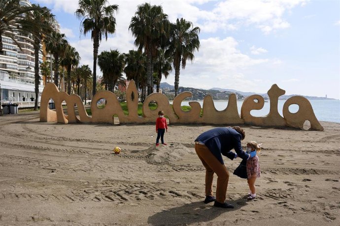 Un hombre junto a sus dos hijos protegidos con mascarilla en la playa de La Malagueta el primer día en el que los menores de 14 años pueden salir, en Málaga (Andalucía ,España) a 26 de abril de 2020.