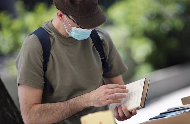 Un hombre protegido con mascarilla observa un libro.