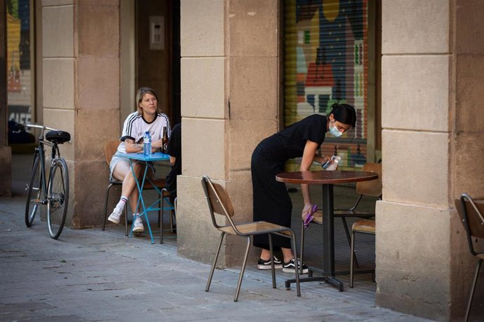 Una camarera limpia varias sillas y una mesa de la terraza de un bar durante el segundo día de la reapertura al público de las terrazas al aire libre, durante el segundo día de la Fase 1 en Barcelona, Catalunya (España) a 26 de mayo de 2020.