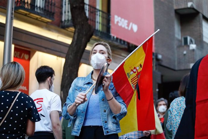 Una mujer con mascarilla sostiene una bandera de España mientras golpea una cacerola en señal de protesta durante la manifestación celebrada en la puerta de la sede del PSOE de la calle Ferraz de Madrid.