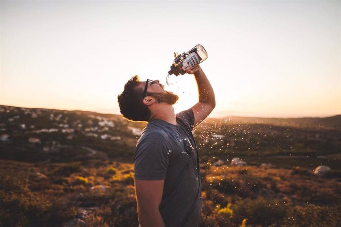 Un hombre  bebe agua de una botella.