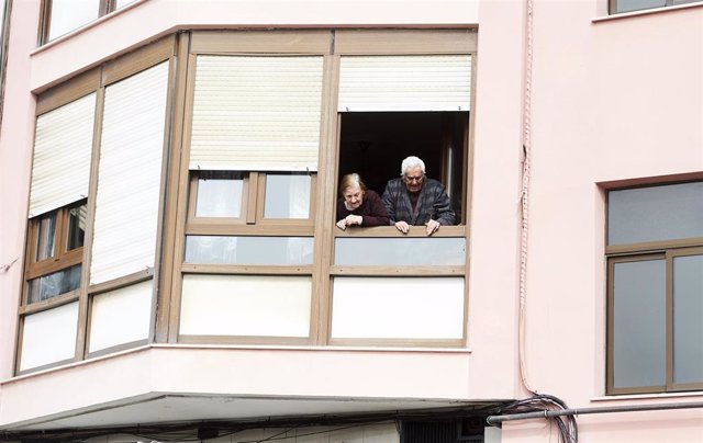 Unos ancianos confinados en sus casas se asoman a su ventana, en Santander (Cantabria, España), a 18 de marzo de 2020.