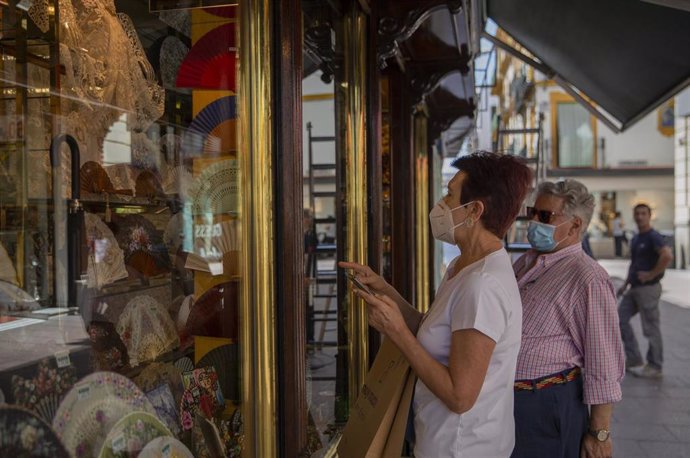 Dos personas con mascarilla observan el escaparate de una tienda durante el tercer día de la fase 2 . En Sevilla, (Andalucía, España), a 27 de mayo de 2020.