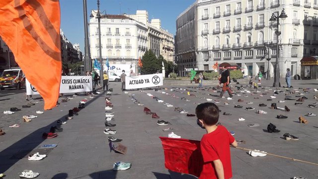 Un niño sostiene una pancarta de Extinction Rebellion en la Puerta del Sol de Madrid, que aparece cubierta de zapatos, en una iniciativa del movimiento internacional de desobediencia civil pacífica en plazas icónicas de varias ciudades españolas exigiendo