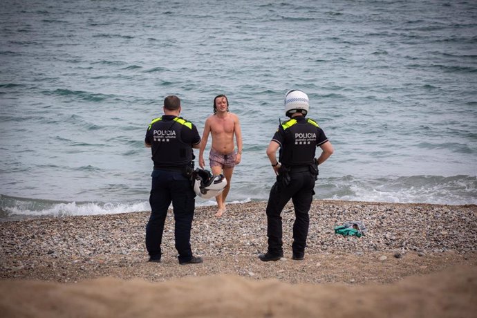 Dos agentes de la Guardia Urbana de Barcelona hablan con un joven que se acaba de bañar en la playa cuando la ciudad está todavía en Fase 1. En Barcelona, Catalunya (España) a 26 de mayo de 2020.