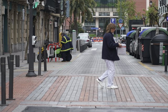 Una sanitaria cruza un paso de cebra mientras un trabajador de Correos continúa trabajando en Bilbao 