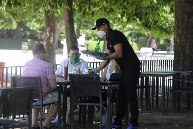 Un camarero protegido con mascarilla atiende a una mesa de una terraza.