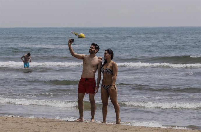 Dos personas se hacen un selfie en la Playa de la Malvarrosa, con bandera verde durante el primer día de la Fase 2, c
