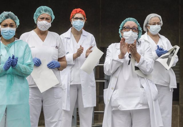 Sanitarios protegidos con mascarillas aplauden conmocionados tras el minuto de silencio en la entrada del Hospital Doctor Peset por la técnica de enfermería fallecida por coronavirus, en Valencia/Comunidad Valenciana (España) a 6 de abril de 2020.