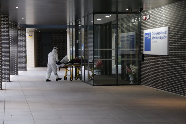 Un sanitario protegido con un traje, guantes y mascarilla, sale con una camilla en la que lleva a una persona. En Vitoria/Euskadi (España) a 18 de marzo de 2020.