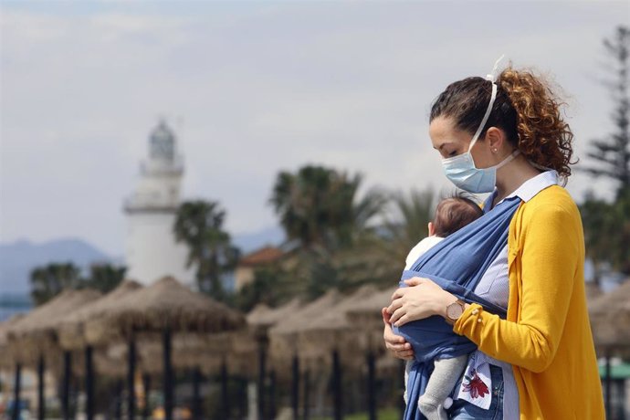 Una mujer protegida con una mascarilla da un paseo con su bebé en la playa de La Malagueta el primer día en el que los menores de 14 años pueden salir, en Málaga (Andalucía ,España) a 26 de abril de 2020.