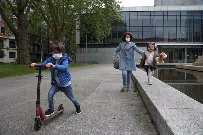 Una mujer pasea junto a una niña y un niño que circula en patinete en el primer día en el que los menores de 14 años pueden salir a la calle, en Bilbao (País Vasco/España) 