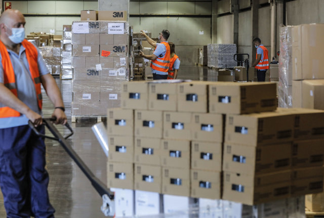 Varias personas trabajan en el centro logístico de Feria Valencia que alberga material sanitario adquirido por la Comunitat Valenciana para la lucha contra la pandemia de COVID-19
