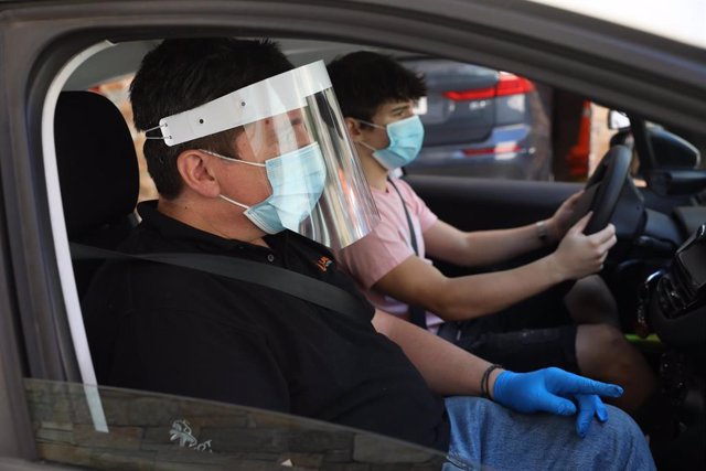 Un profesor de autoescuela y su alumno, en una clase práctica del carné de conducir, protegidos con mascarillas, guantes y viseras para protegerse del coronavirus