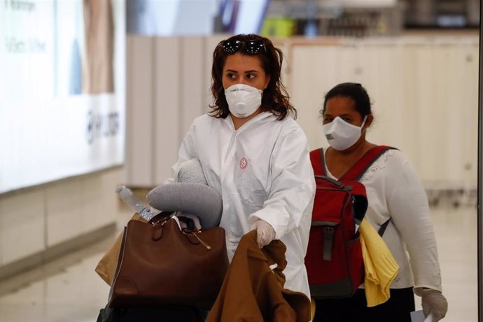 Una mujer protegida con mascarilla y traje EPI pasa los controles en la terminal 4 del Aeropuerto de Madrid-Barajas Adolfo Suárez