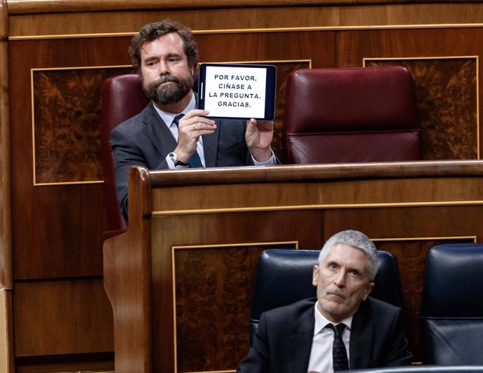 El diputado de VOX Iván Espinosa de los Monteros sostiene un cartel detrás del ministro del Interior, Fernando Grande-Marlaska