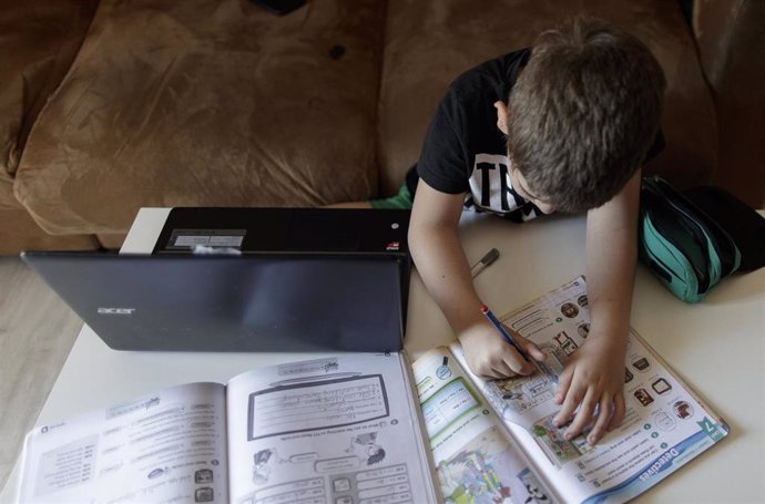 Un alumno de primaria hace los deberes con varios libros y un ordenador 