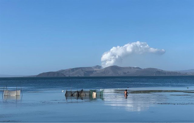 FILED - 16 January 2020, Philippines, Lake Taal: A man wades through the waters of Lake Taal as ash and steam rise from the crater of Taal Volcano.  