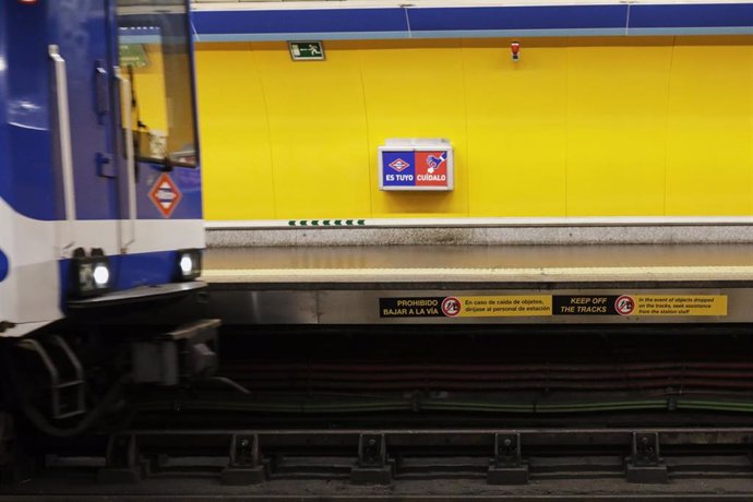 Un tren de metro entra en una estación en la que se ve uno de los carteles que la Comunidad de Madrid ha instalado a lo largo del borde del andén en las estaciones del Metro de Madrid.