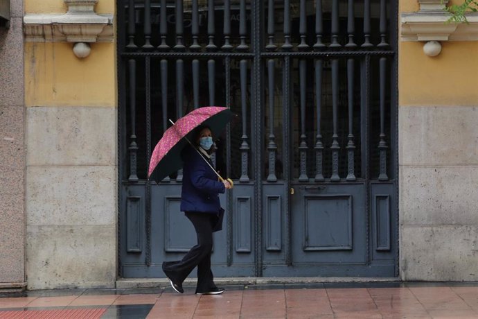 Una mujer pasa frente a una puerta en la capital en un día de lluvia y bajada de temperaturas en toda España