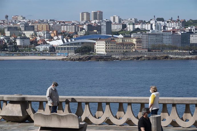 Dos personas pasean por el paseo marítimo de A Coruña (Galicia), con el estadio de Riazor de fondo, en el segundo día en que el Gobierno permite salir a hacer deporte de forma individual y pasear con otra persona con la que se conviva, a determinadas ho