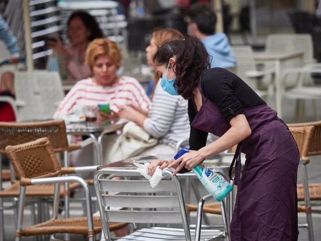 Una trabajadora desinfecta las mesas y sillas de una terraz.