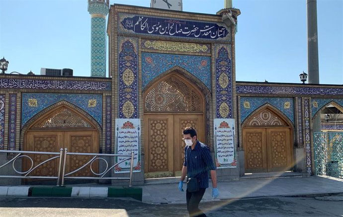 Un hombre con mascarilla camina frente a una mezquita en Teherán