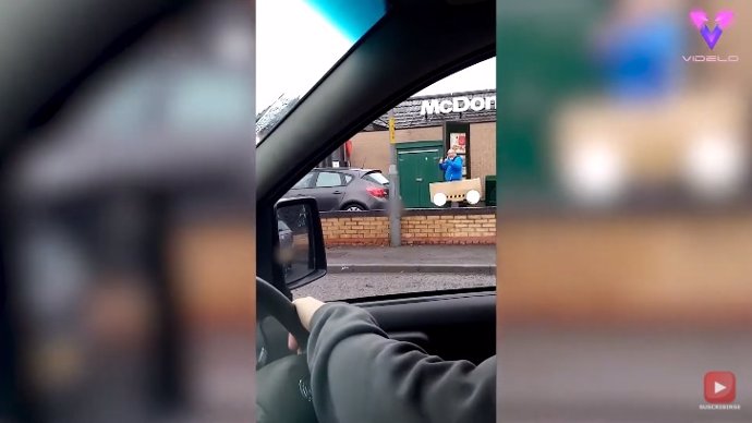 Graban a un hombre haciendo cola en el autoservicio de un Mc Donalds en un coche de cartón