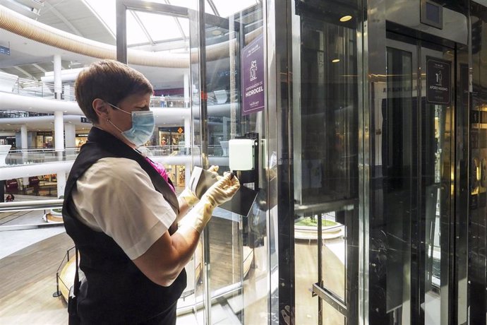 Una trabajadora de la limpieza coloca un recambio de gel desinfectante en un dispensador del Centro comercial Vallsur