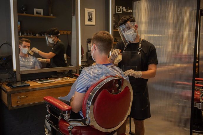Un peluquero atiende a un cliente durante la fase 0 de la desescalada. En Barcelona, Cataluña, (España), a 5 de mayo de 2020.