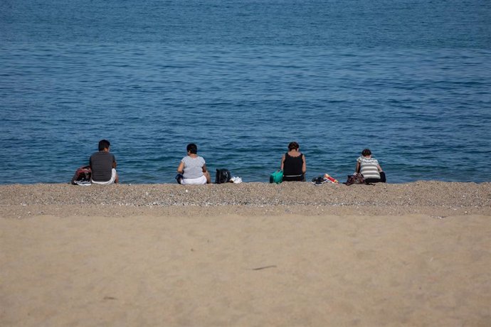 Varias personas sentadas en la Playa de la Barceloneta respetan la distancia de seguridad