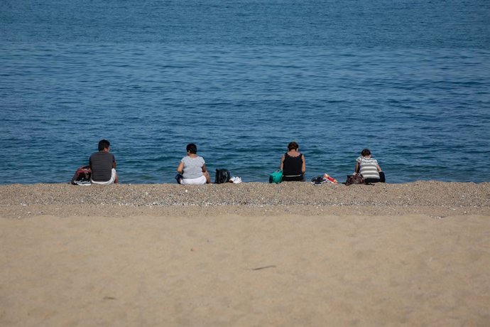 Diverses persones assegudes a la Platja de la Barceloneta respecten la distncia de seguretat