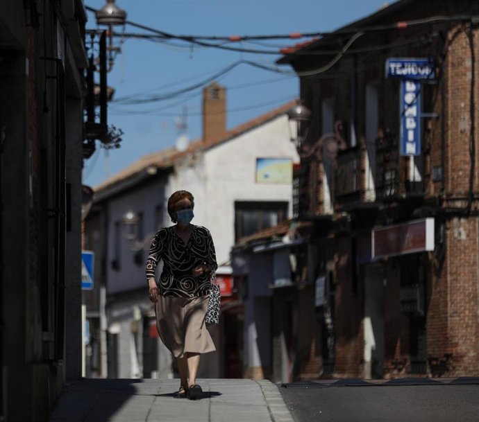 Una mujer protegida con mascarilla anda por una calle del pueblo madrileño de Algete durante el día 68 del Estado de Alarma