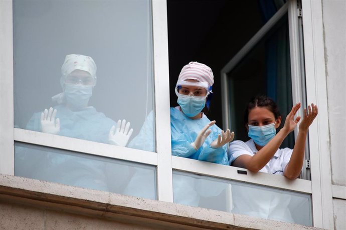 Varios sanitarios con protección EPI, mascarillas, gafas y guantes, aplauden en agradecimiento desde la ventana el homenaje a los Sanitarios celebrado en el Hospital Fundación Jiménez Díaz durante la pandemia de COVID-19